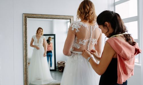 Assistant buttoning up a wedding dress
